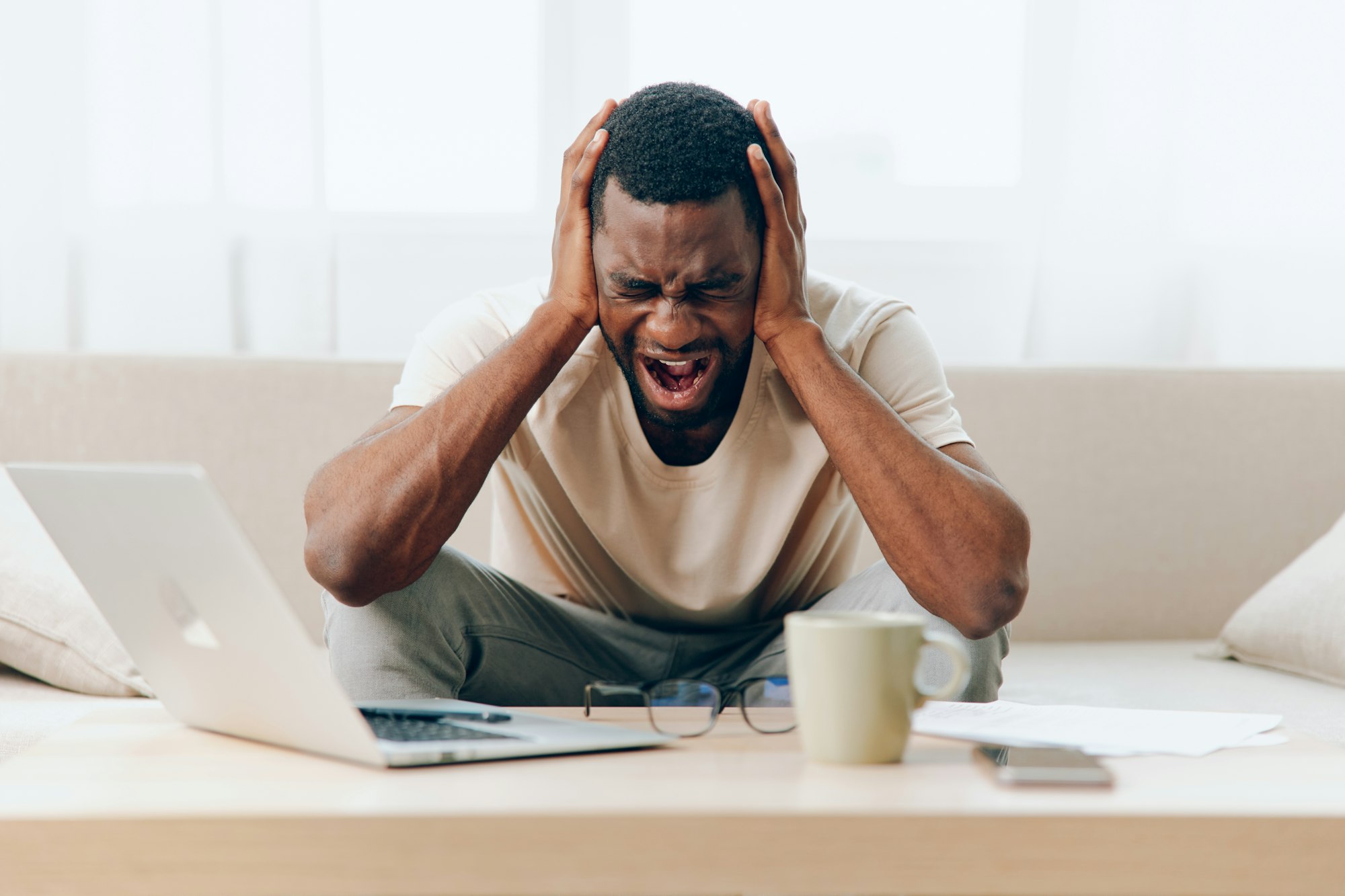 Tired African American Man Working on Laptop in a Depressed State on the Sofa in a Modern Home